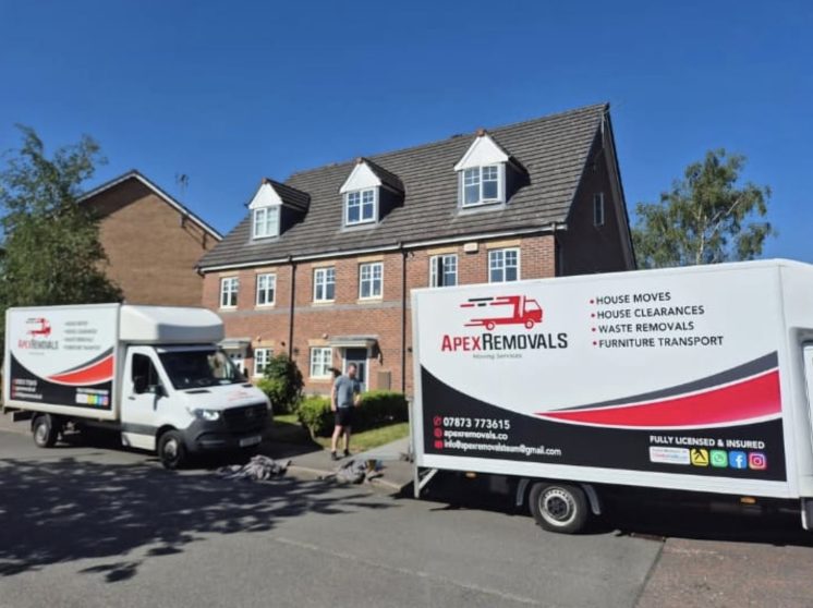 Two Apex Removals vans and a team member outside a large detached brick house on move day